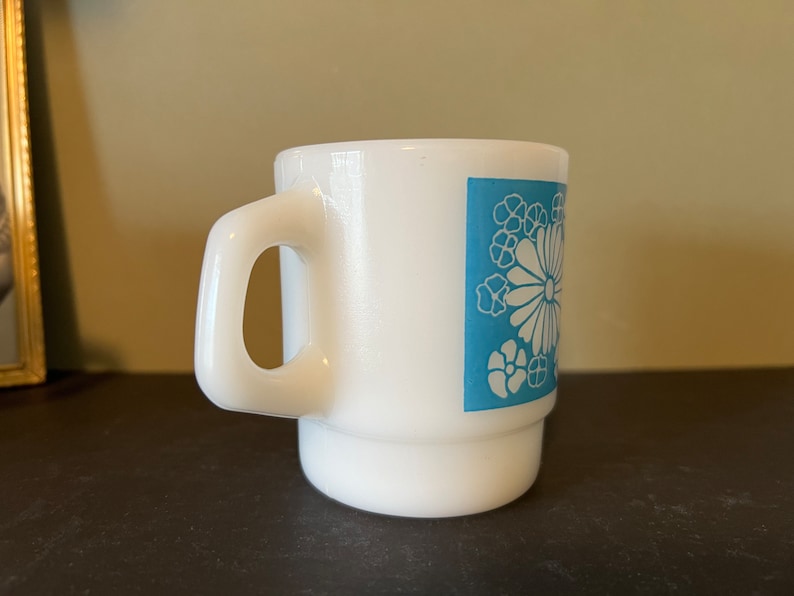 May include: White ceramic mug with a blue floral design. The mug has a handle and a wide base.