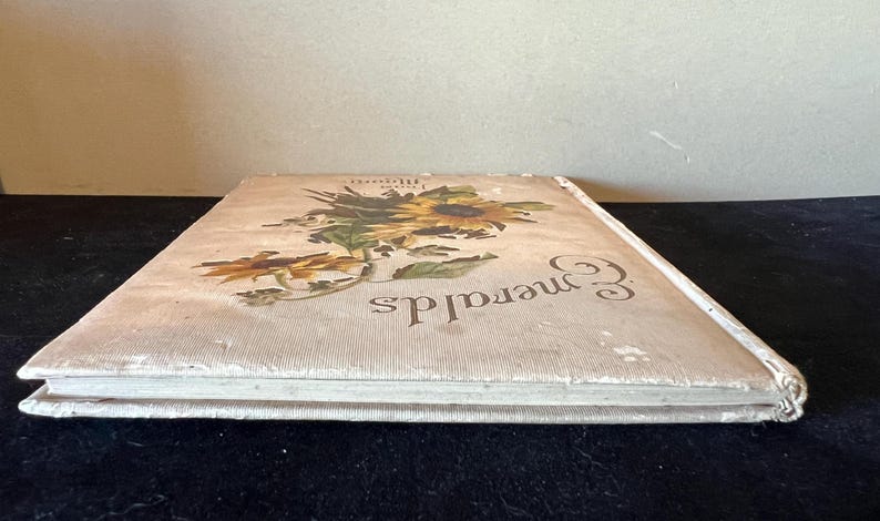 May include: A white book with a floral design on the cover. The book is titled "Emeralds" and has a white spine.
