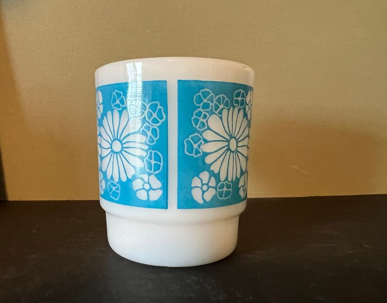 May include: White ceramic mug with a blue and white floral pattern. The mug has a wide base and a rounded top.