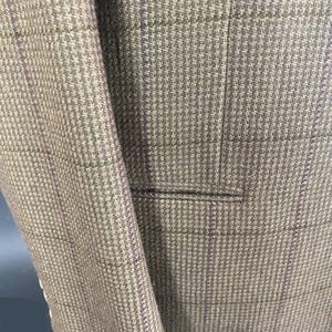 May include: Close-up of a tweed blazer in shades of brown and gray with a subtle purple plaid pattern. The jacket features a notched lapel and a pocket, showcasing the tailored design and textured fabric.