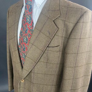 May include: A brown blazer with a subtle plaid pattern, paired with a white dress shirt and a patterned tie featuring red and blue paisley designs. The blazer has a single-button closure and a chest pocket.