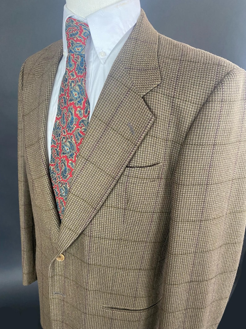 May include: A brown blazer with a subtle plaid pattern, paired with a white dress shirt and a patterned tie featuring red and blue paisley designs. The blazer has a single-button closure and a chest pocket.