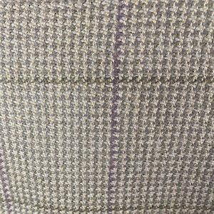 May include: Close-up of a textured fabric with a houndstooth pattern in shades of beige, gray, and a thin purple stripe. The weave is tight, creating a detailed and visually interesting surface. The fabric appears to be a woven material, possibly wool or a wool blend.