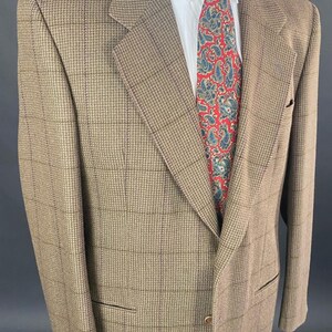 May include: A brown and tan plaid blazer with a white dress shirt and a red paisley tie. The blazer has a classic cut with a notched lapel and two front pockets. The tie features a blue and white paisley pattern.
