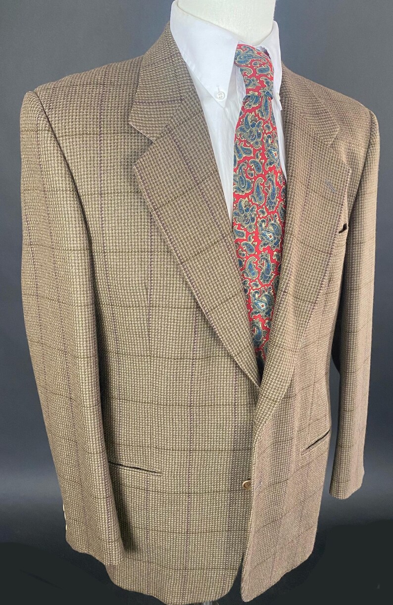 May include: A brown and tan plaid blazer with a white dress shirt and a red paisley tie. The blazer has a classic cut with a notched lapel and two front pockets. The tie features a blue and white paisley pattern.