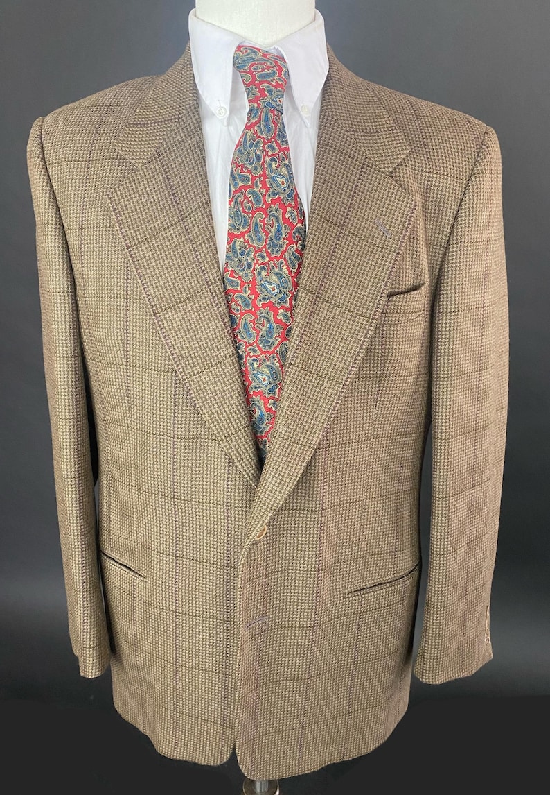 May include: A brown plaid blazer with a white collared shirt and a red paisley tie. The blazer has a classic fit with a notched lapel and two front pockets. The tie features a blue and white paisley pattern.