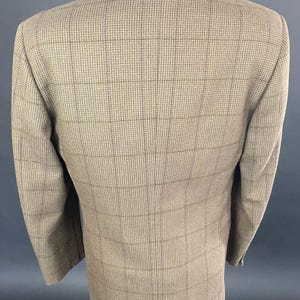 May include: A tan blazer with a plaid pattern. The jacket has a classic design with a notched lapel and two buttons. The fabric appears to be a woven material, and the blazer is displayed on a mannequin.