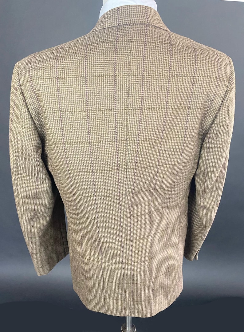 May include: A tan blazer with a plaid pattern. The jacket has a classic design with a notched lapel and two buttons. The fabric appears to be a woven material, and the blazer is displayed on a mannequin.