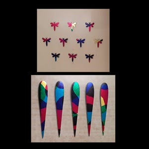Puede incluir: La imagen muestra dos conjuntos de elementos decorativos. La sección superior presenta pequeñas formas de libélulas metálicas en varios colores. La sección inferior muestra cinco piezas de madera alargadas pintadas con patrones abstractos coloridos, incluyendo rojo, azul y verde.