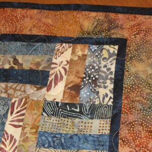 Peut inclure: Un chemin de table en patchwork avec un motif bleu et brun. Le chemin de table est compos&eacute; de diff&eacute;rents morceaux de tissu cousus ensemble dans un motif g&eacute;om&eacute;trique. Les bords sont bord&eacute;s d'un tissu bleu fonc&eacute;.
