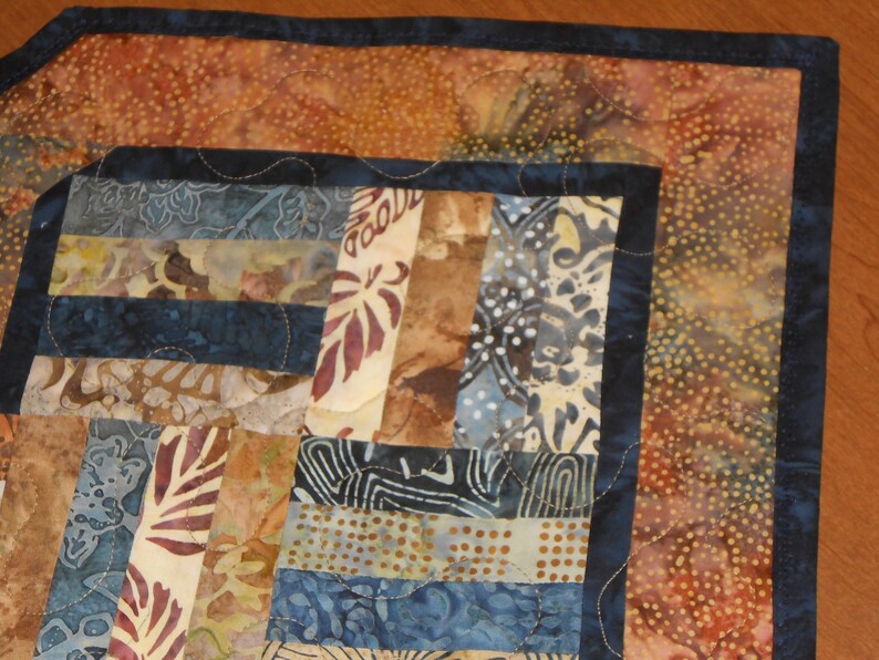 Peut inclure: Un chemin de table en patchwork avec un motif bleu et brun. Le chemin de table est compos&eacute; de diff&eacute;rents morceaux de tissu cousus ensemble dans un motif g&eacute;om&eacute;trique. Les bords sont bord&eacute;s d'un tissu bleu fonc&eacute;.