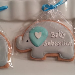 May include: Two decorated sugar cookies shaped like elephants. One cookie is light blue with the text "It's a Boy!" and a blue heart. The other cookie is light blue with the text "Baby Sebastian" and a blue heart.