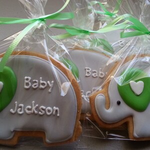 May include: Three gray elephant-shaped cookies decorated with green icing and a white heart. Each cookie is individually packaged in a clear plastic bag with a green ribbon and says "Baby Jackson" in white icing.