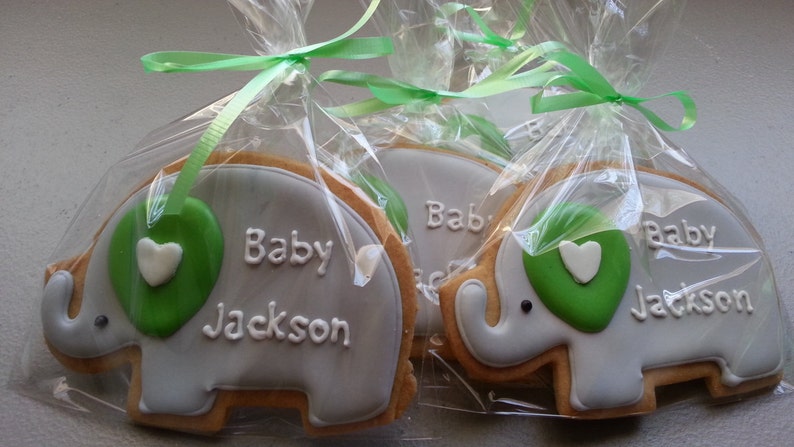 May include: Three gray elephant-shaped cookies decorated with green icing and a white heart. Each cookie is individually packaged in a clear plastic bag with a green ribbon and says "Baby Jackson" in white icing.