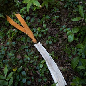 May include: A rectangular bookmark made from a piece of white antler with a rough, porous texture on the front surface. A tan suede leather cord is attached to the top of the antler piece through a small hole, tied in a simple knot.