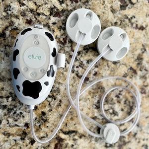 May include: A white and black cow print electric breast pump with a control panel that says "elvie" and two white flanges connected to clear tubes.