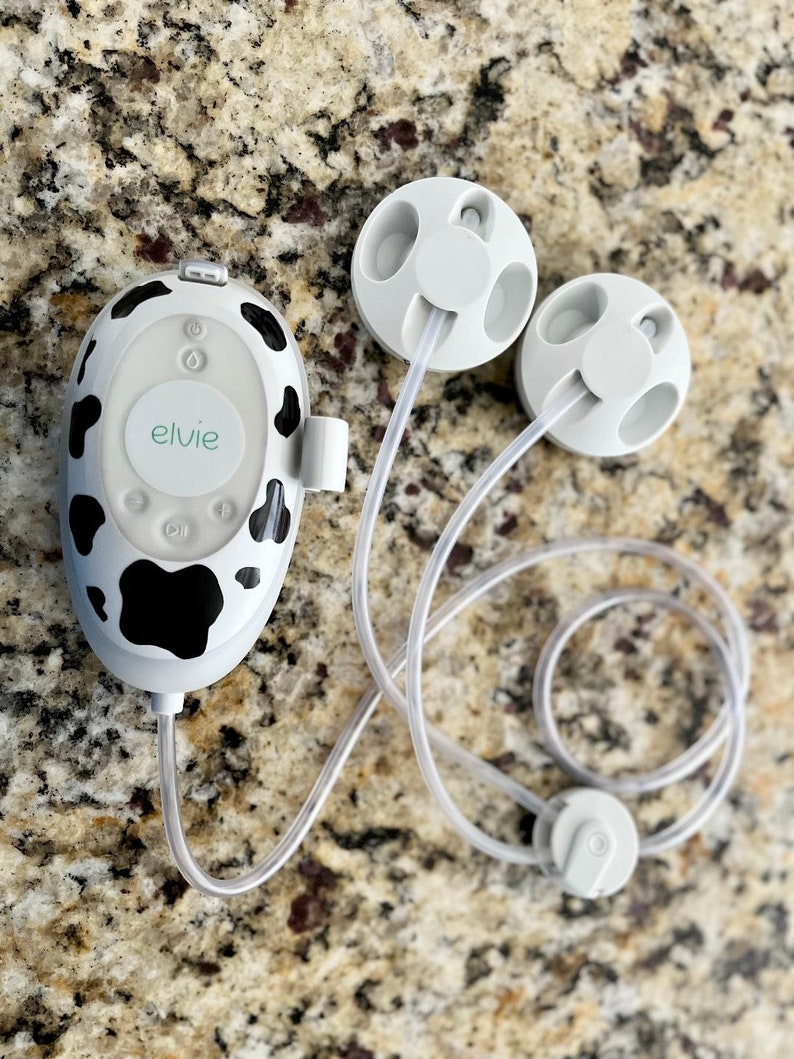 May include: A white and black cow print electric breast pump with a control panel that says "elvie" and two white flanges connected to clear tubes.