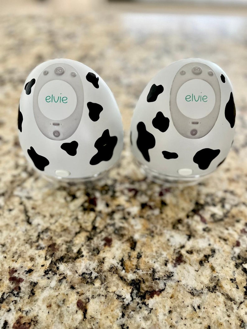 May include: Two white and black cow print electric breast pumps with the word "elvie" on the front.