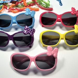 Puede incluir: Cinco pares de gafas de sol con diferentes marcos y lazos de colores. Las gafas de sol tienen lentes oscuras y est&aacute;n todas enfocadas. Los lazos son de diferentes colores y tienen lunares blancos.