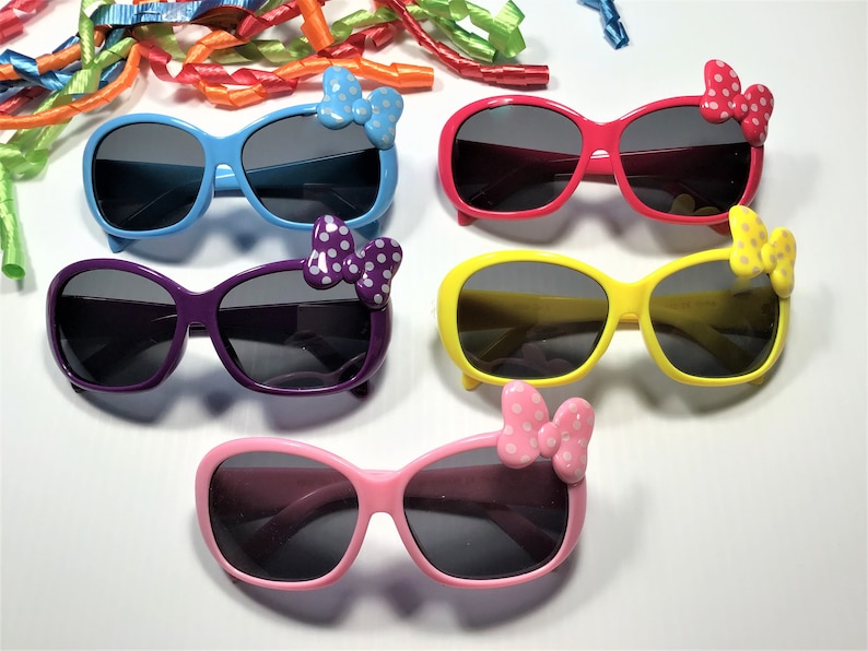 Puede incluir: Cinco pares de gafas de sol con diferentes marcos y lazos de colores. Las gafas de sol tienen lentes oscuras y est&aacute;n todas enfocadas. Los lazos son de diferentes colores y tienen lunares blancos.