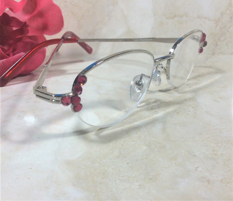 Pu&ograve; includere: Occhiali con montatura argentata, dettagli rossi e lenti trasparenti. Le montature presentano abbellimenti rossi e sono accentuati da aste rosse. Gli occhiali hanno un design moderno ed elegante, adatti all'uso quotidiano.
