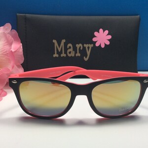 May include: Black sunglasses with pink frames and mirrored lenses. The sunglasses are in a black case with the name "Mary" and a pink flower printed on it.