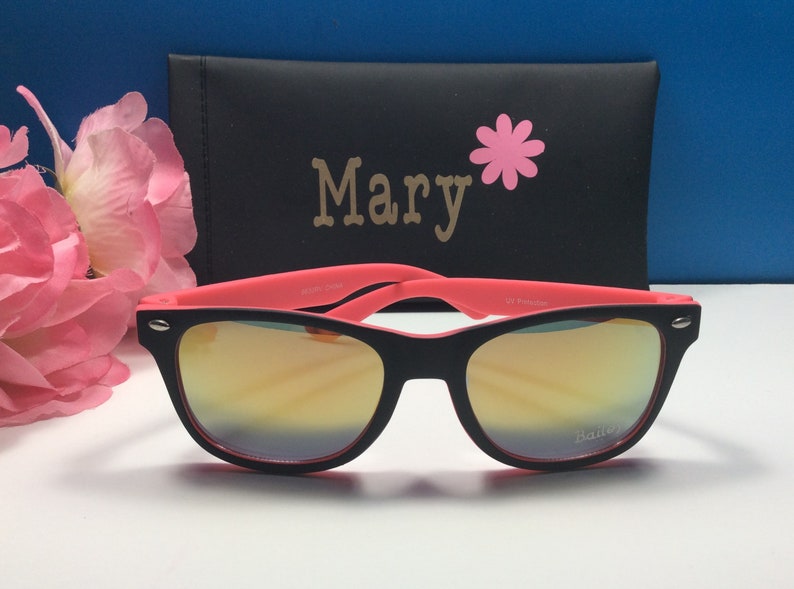 May include: Black sunglasses with pink frames and mirrored lenses. The sunglasses are in a black case with the name "Mary" and a pink flower printed on it.