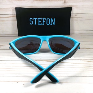K&ouml;nnte beinhalten: Blaue und schwarze Sonnenbrille mit einem schwarzen Etui, auf dem "STEFON" steht.