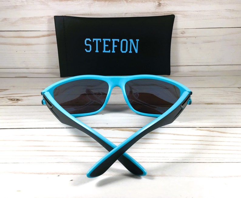 K&ouml;nnte beinhalten: Blaue und schwarze Sonnenbrille mit einem schwarzen Etui, auf dem "STEFON" steht.