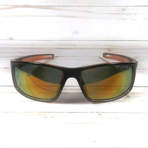 May include: Black sunglasses with orange and green reflective lenses. The frames are black with orange accents on the arms. The lenses have a polarized coating. The sunglasses are set against a white wooden background.