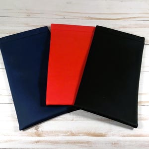 Pode incluir: Tr&ecirc;s bolsas de tecido em azul marinho, vermelho e preto. As bolsas est&atilde;o dobradas e empilhadas umas sobre as outras.