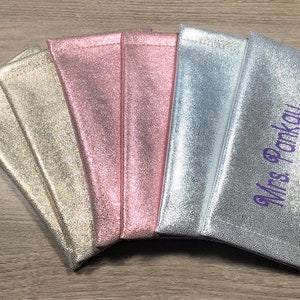 Pu&ograve; includere: Una collezione di pochette metallizzate nei toni dell'oro, del rosa e dell'argento, disposte su una superficie di legno. Una pochette &egrave; ricamata con il nome "Mrs Pankau" in viola.