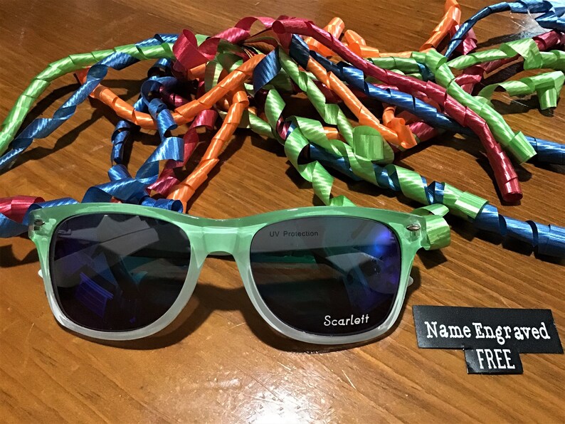 May include: Green sunglasses with UV protection and the name "Scarlett" engraved on the right lens. A black and white label reads "Name Engraved FREE".