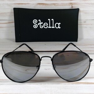 May include: Black aviator sunglasses with mirrored lenses and a black case with the word "Stella" printed in white.