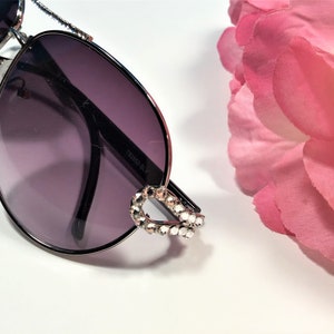 May include: Silver aviator sunglasses with dark grey lenses and a rhinestone detail on the frame.