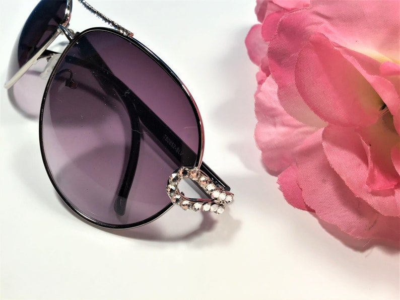 May include: Silver aviator sunglasses with dark grey lenses and a rhinestone detail on the frame.