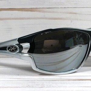May include: Black and silver wraparound sunglasses with a mirrored lens. The sunglasses have a black logo on the side.