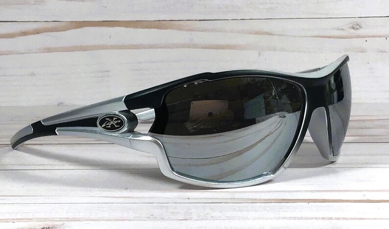 May include: Black and silver wraparound sunglasses with a mirrored lens. The sunglasses have a black logo on the side.