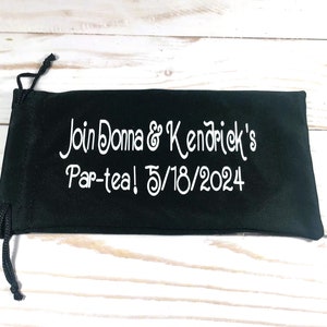 May include: Black velvet drawstring bag with white embroidery that reads "Join Donna & Kendrick's Par-tea! 5/18/2024"