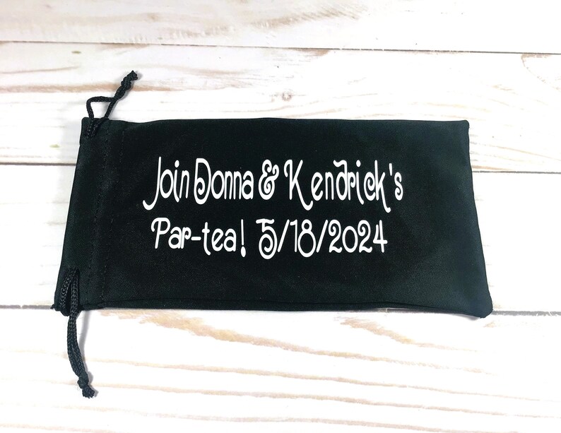 May include: Black velvet drawstring bag with white embroidery that reads "Join Donna & Kendrick's Par-tea! 5/18/2024"