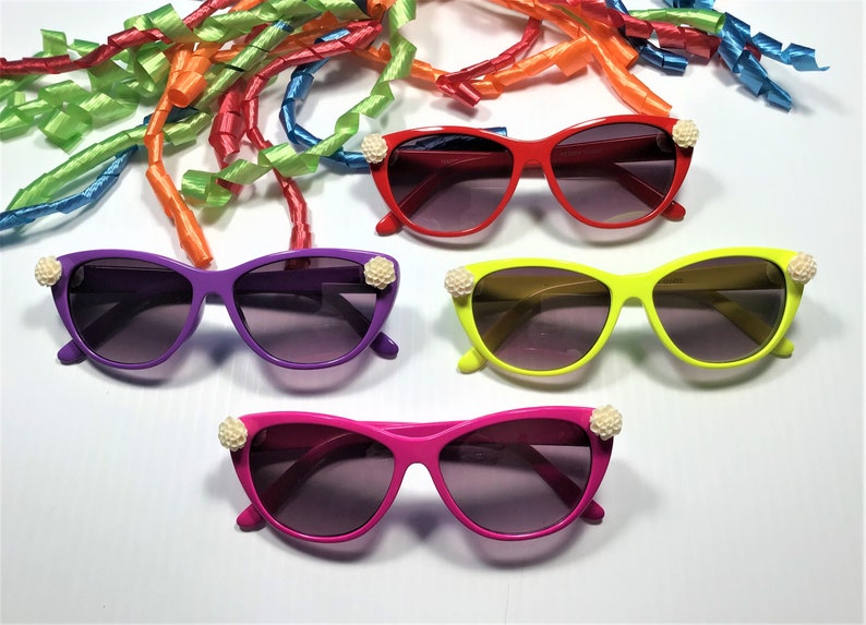 May include: Four pairs of colourful cat-eye sunglasses with white pearl accents. The sunglasses are in red, purple, yellow, and pink.