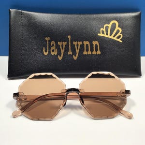 May include: Brown octagon-shaped sunglasses with a black frame and a black case with the name "Jaylynn" printed in gold letters.