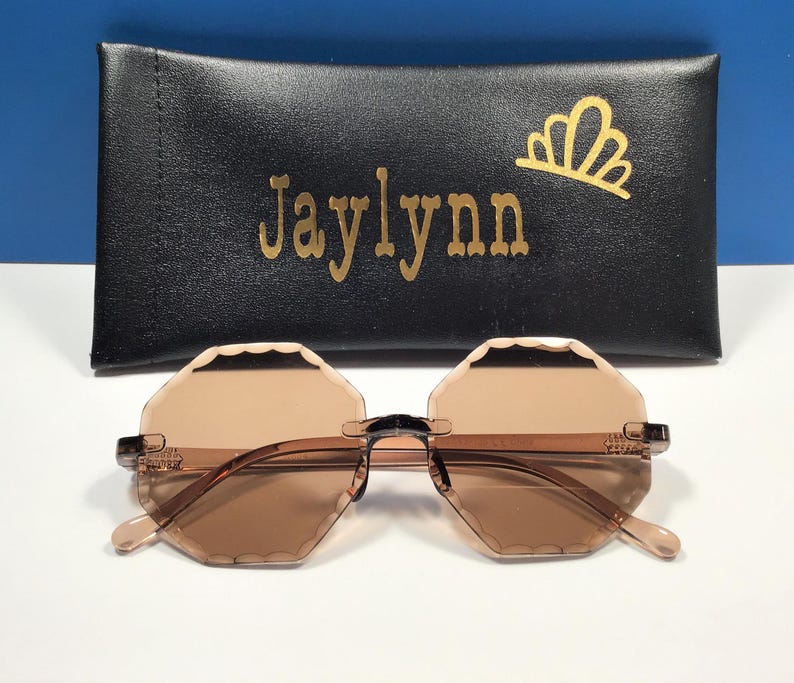 May include: Brown octagon-shaped sunglasses with a black frame and a black case with the name "Jaylynn" printed in gold letters.