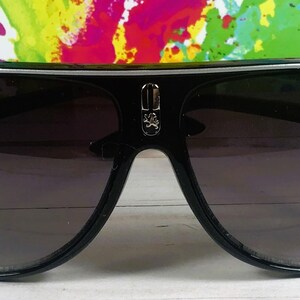 Puede incluir: Gafas de sol de aviador negras con ribete plateado y lentes degradadas. Las gafas de sol tienen un emblema decorativo en el puente y el nombre "Kian" impreso en la lente.