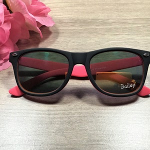May include: Black sunglasses with pink accents and a "Bailey" label on the right lens. The sunglasses have UV protection.