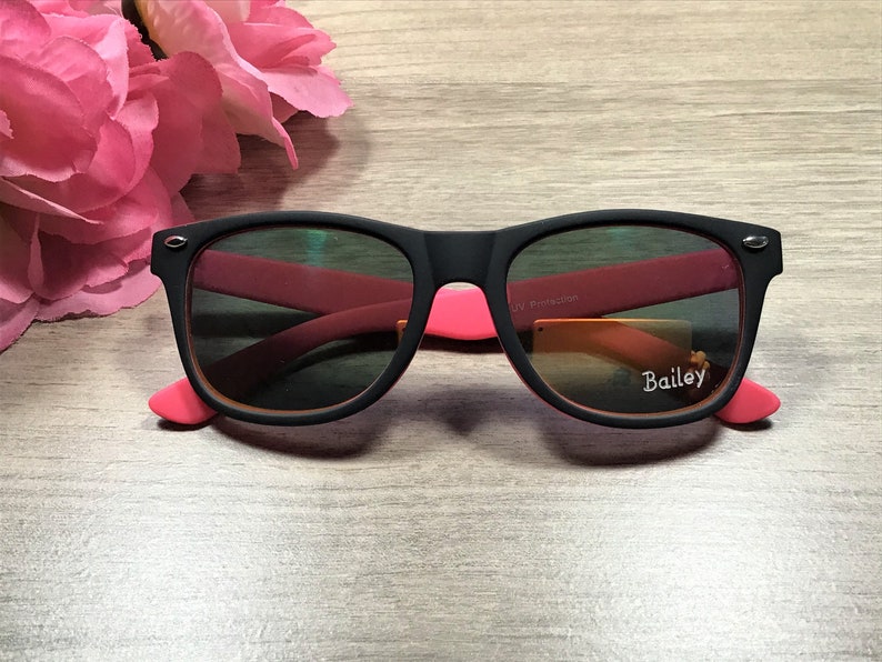 May include: Black sunglasses with pink accents and a "Bailey" label on the right lens. The sunglasses have UV protection.
