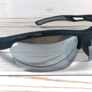 May include: Matte black sports sunglasses featuring a wraparound frame design with silver mirrored lenses. The temples display a small rectangular logo plate on the side, and the frame includes ventilation cutouts along the top brow bar.
