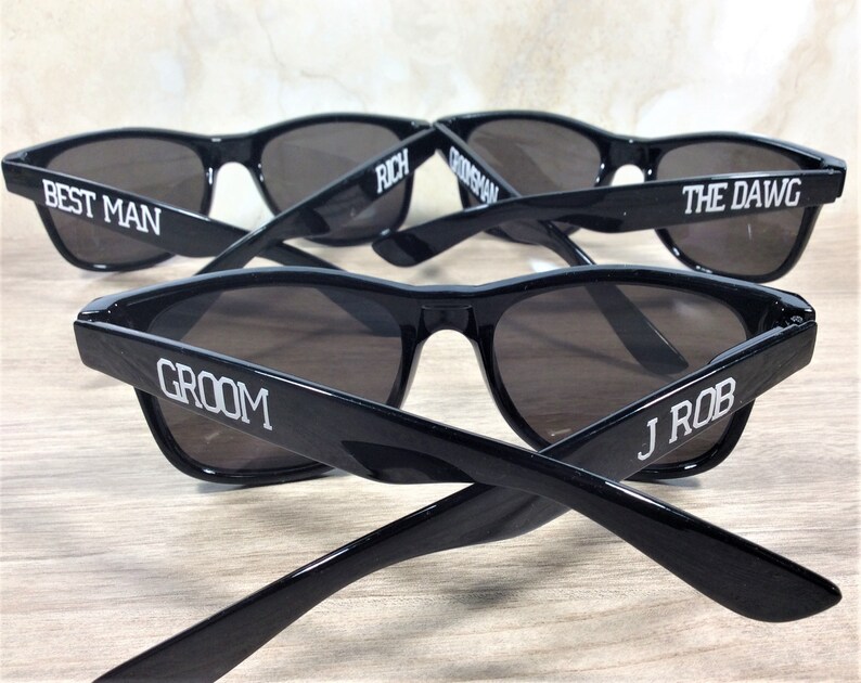 May include: Five black sunglasses with white text on the frames. The text reads "Best Man", "Groom", "Rich", "The Dawg", and "J Rob".