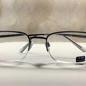 May include: Black rimmed reading glasses with a +3.00 power lens. The glasses have a half-frame design with decorative black beads on the upper corners. The lenses are clear, and the frame is a thin, dark metal.