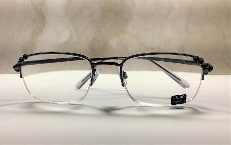 May include: Black rimmed reading glasses with a +3.00 power lens. The glasses have a half-frame design with decorative black beads on the upper corners. The lenses are clear, and the frame is a thin, dark metal.